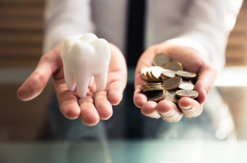 Person holding a tooth model and coins representing the cost of gum disease treatment in Vaughan