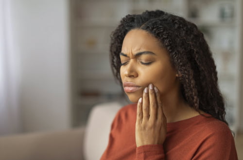 Patient holding her cheek due to a severe toothache, illustrating a situation that may require emergency dental treatment in Vaughan