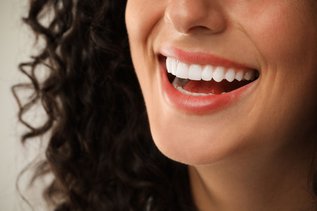 Smiling woman with healthy white teeth on a light grey background representing cosmetic dentistry services in Vaughan