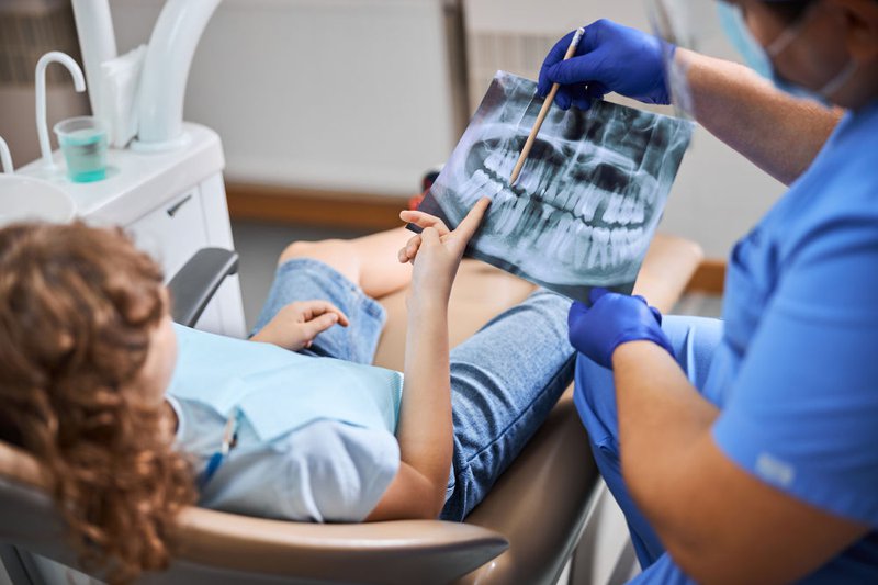 A dentist pointing to an X-ray image while explaining whether a molar requires a root canal or tooth extraction.