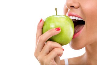 Woman biting into a green apple, showing a hard food that can damage a dental crown