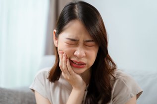 A woman holding her cheek in pain, showing early symptoms of tooth infection that may require a root canal or extraction.