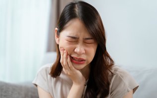 A woman holding her cheek in pain, showing early symptoms of tooth infection that may require a root canal or extraction.