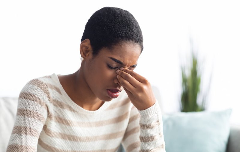 Young woman touching her forehead, experiencing sinus pressure that mimics ta toothache
